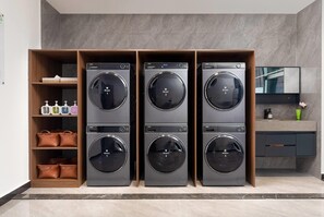 A laundry room with three stacked washer-dryer units, a shelf with toiletries, and a mirror above the units. - Wyndham Garden Changsha Economic Development Zone (Changsha)