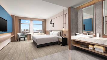 Een moderne hotelkamer met een groot bed, een bureau, een stoel, een televisie, een badkamer met spiegel en wastafel, en uitzicht op de stad.