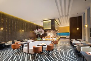 Un hall d’hôtel moderne avec une table de salle à manger ronde, des espaces de détente et un mur décoratif orné de texte vertical.