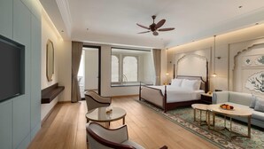 A hotel room with a bed, a sofa, a dining table, a TV, and a ceiling fan. - Wyndham Garden Udaipur Bhuwana (Udaipur)