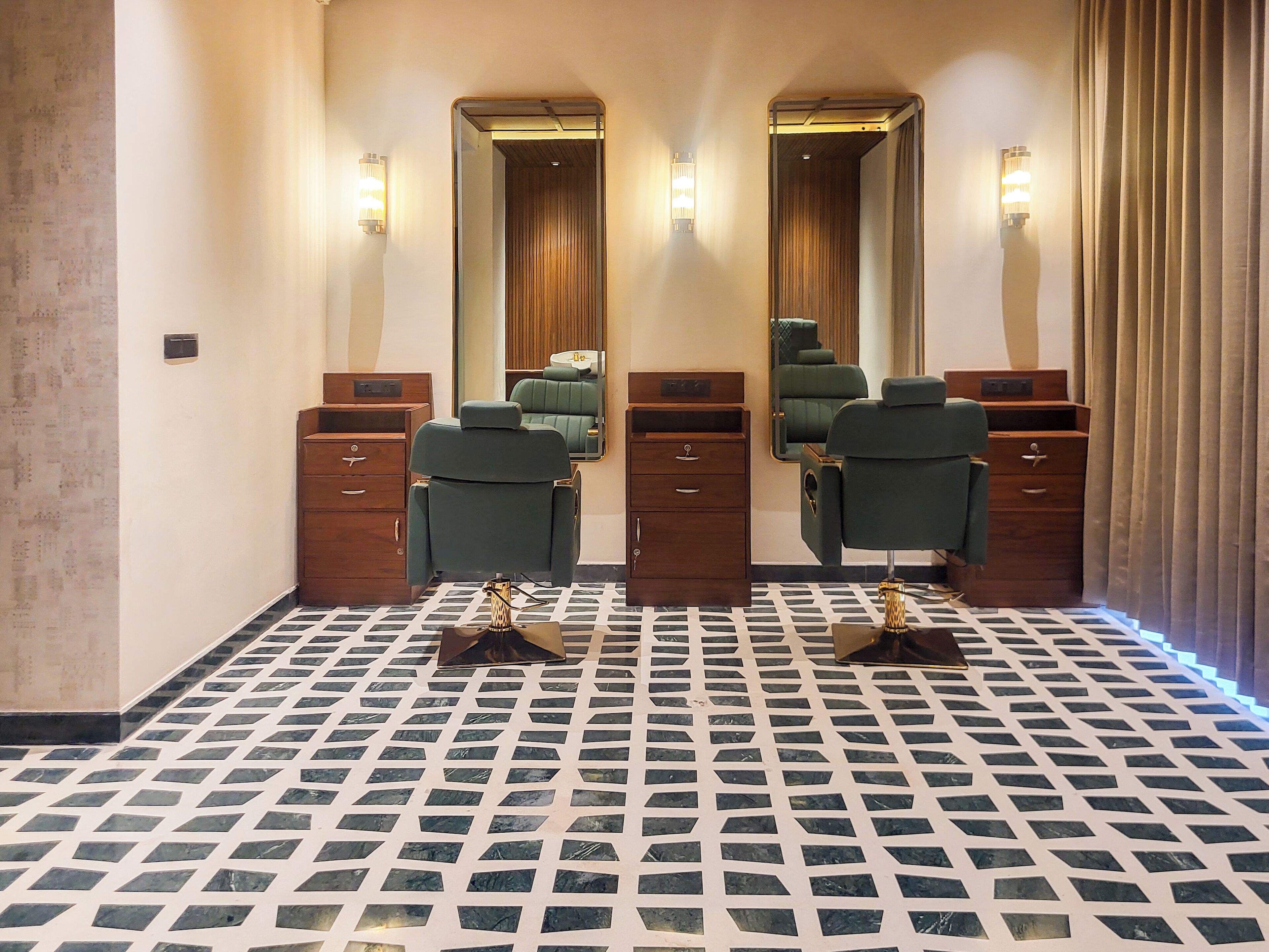 A room with two mirrors, a green salon chair, wooden cabinets, and a patterned floor.