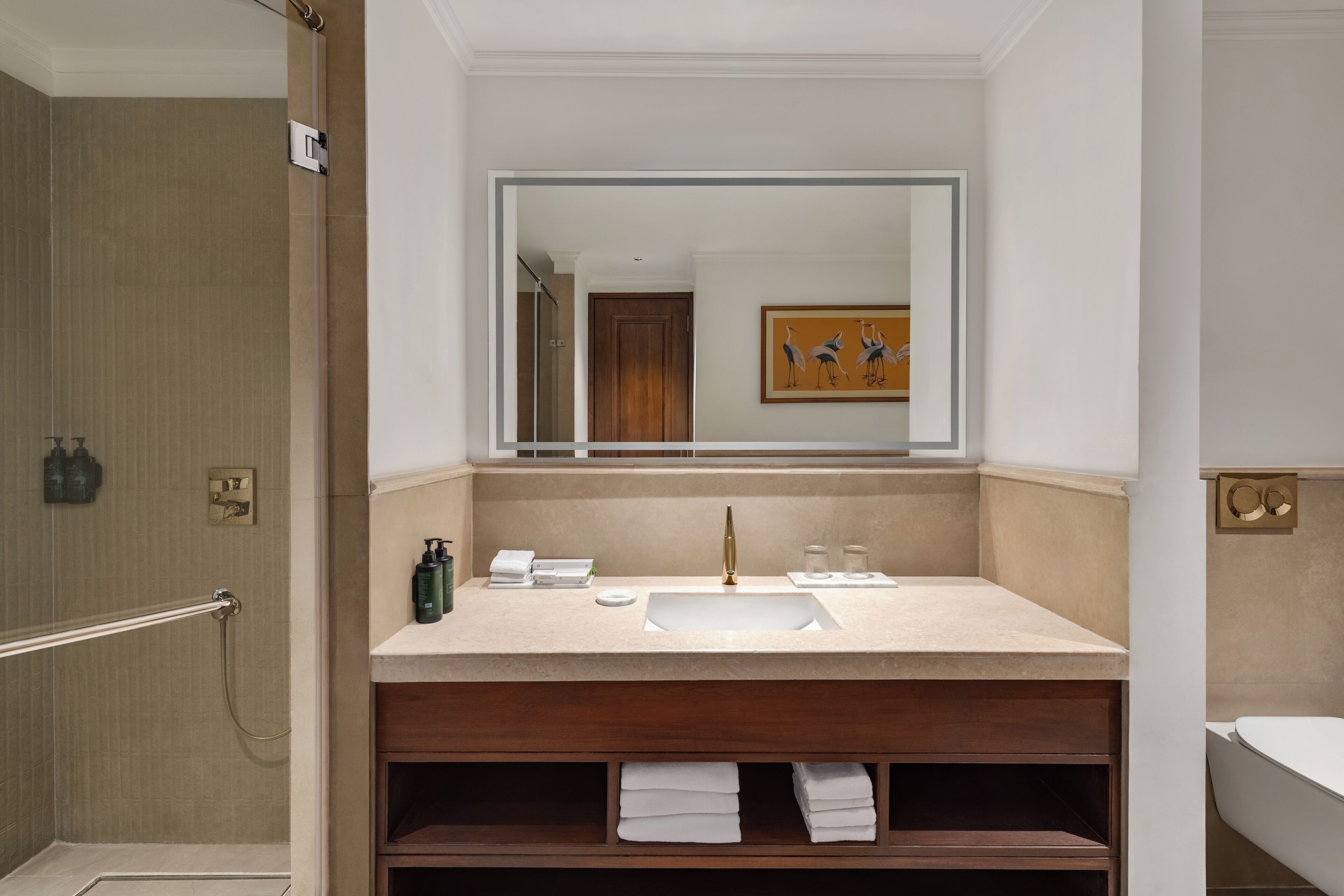 Un baño con un espejo grande, un lavabo, una ducha y un mueble de tocador de madera con toallas.