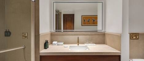 Un baño con un espejo grande, un lavabo, una ducha y un mueble de tocador de madera con toallas.