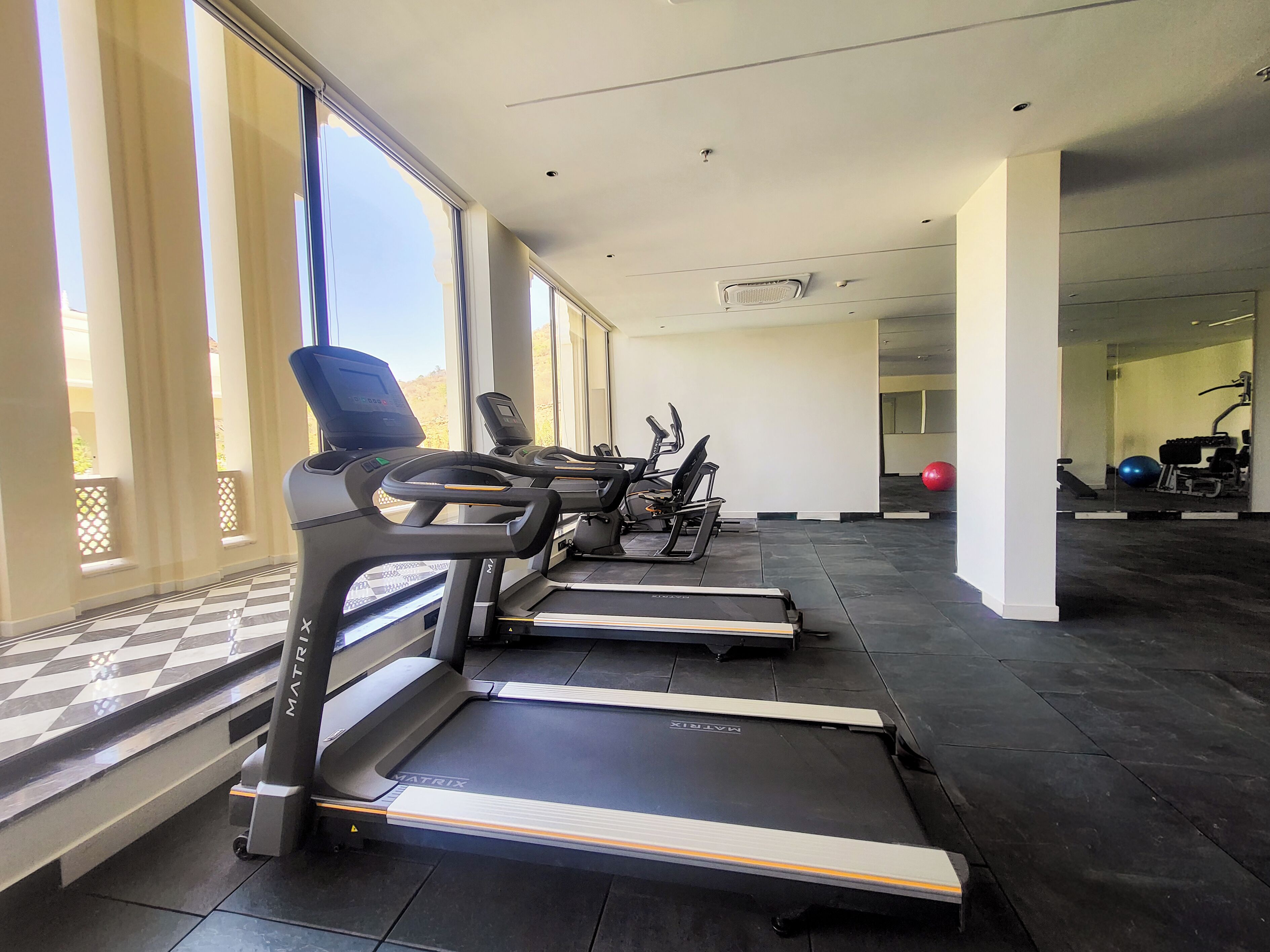 A gym with treadmills, exercise bikes, and a red exercise ball.