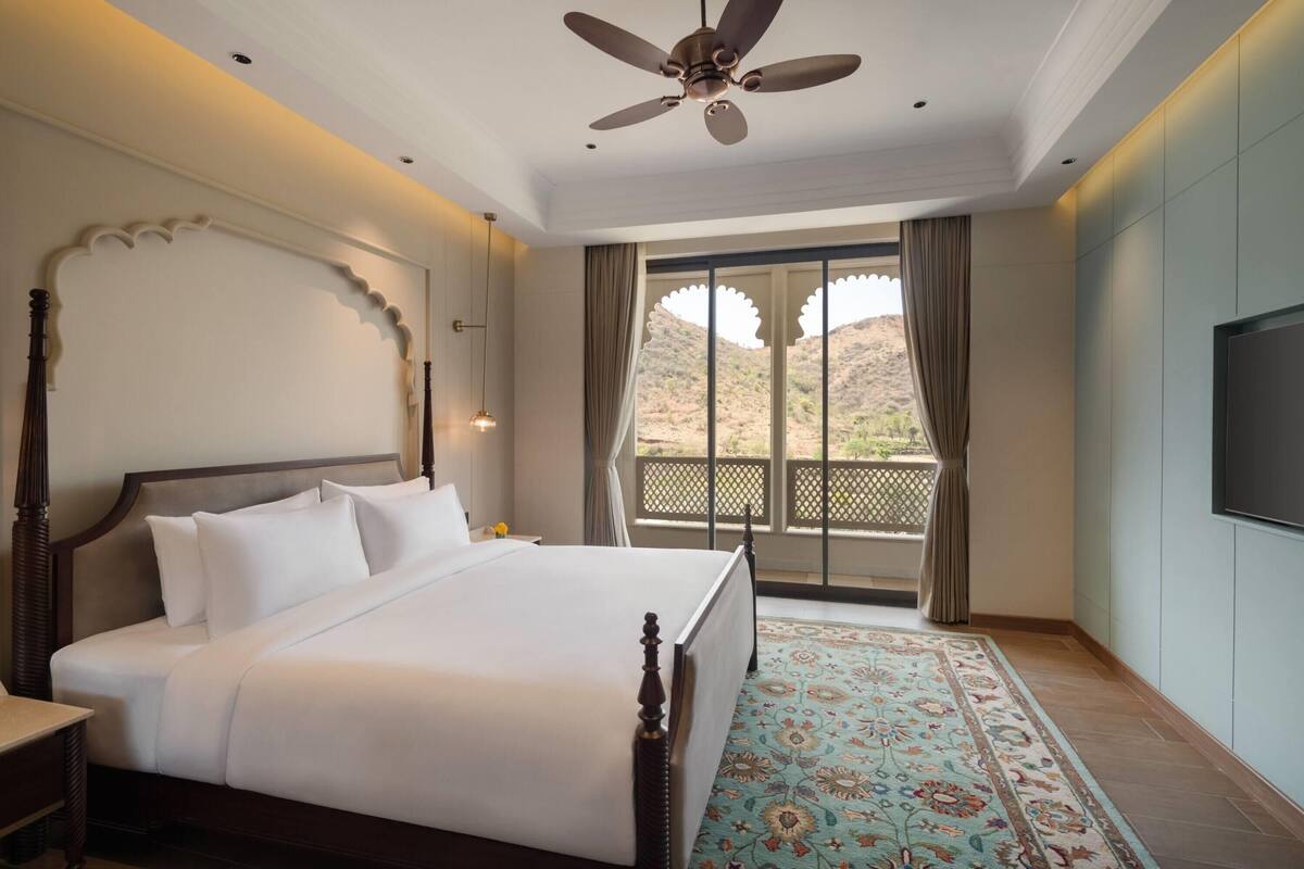 Un dormitorio con cama, ventilador de techo, televisor y vista al exterior.