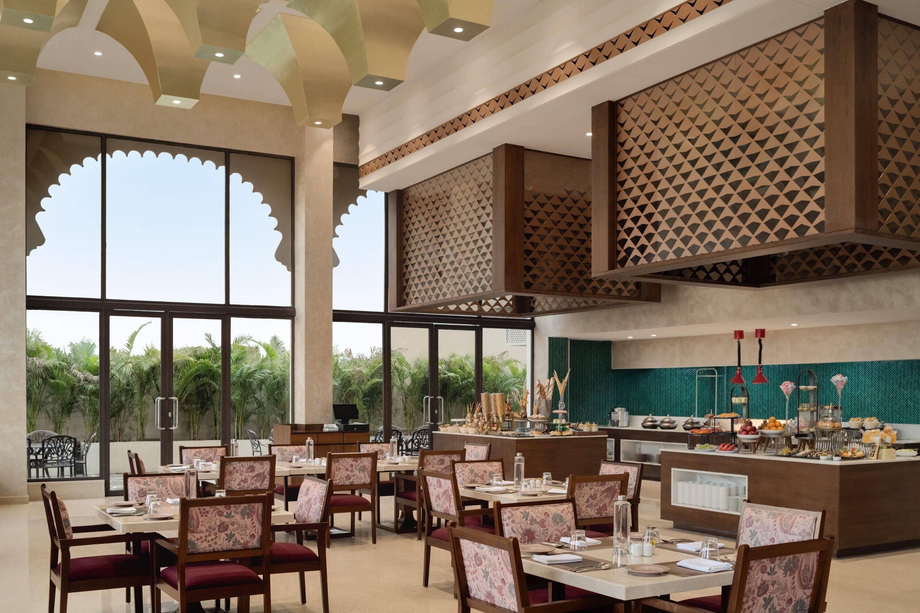 Un ristorante con diversi tavoli e sedie, un'area buffet e ampie finestre che offrono vista sul verde.