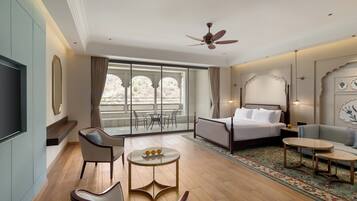Habitación de hotel con cama, sofá, televisor, ventilador de techo y balcón con vistas.