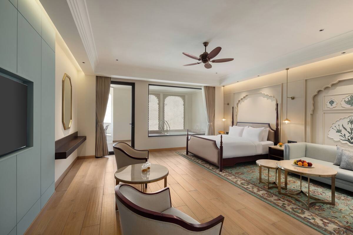 Habitación de hotel con cama, sofá, mesa de comedor, televisión y ventilador de techo.