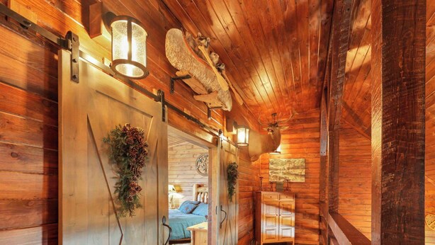 A wooden cabin interior with a bed, a dining area, and a large deer head mounted on the wall. - Luxury Secluded Lodge with a View | Hot Tub•Games (Logan)
