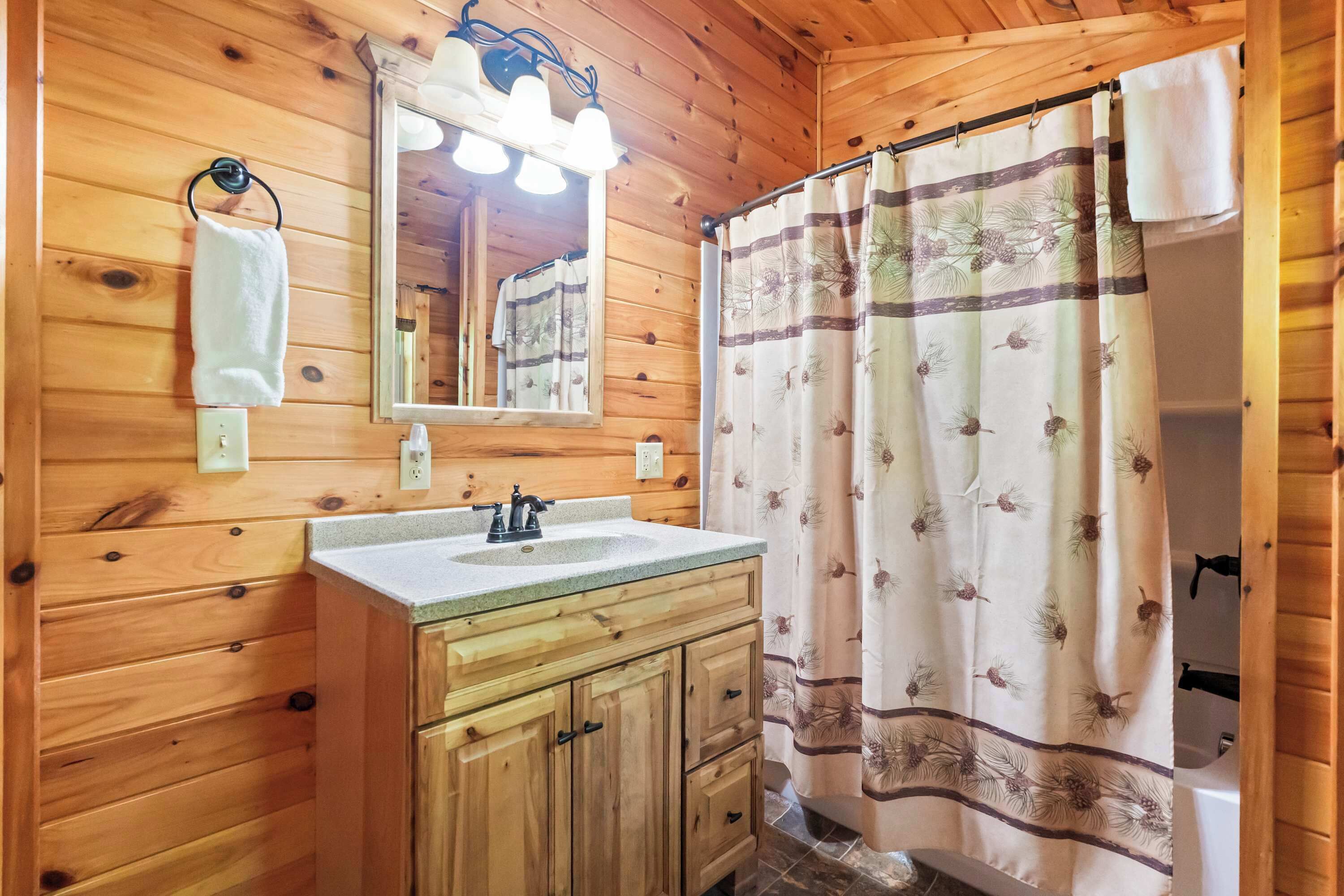 Une salle de bain rustique, avec des murs en bois, comprenant un lavabo, un miroir et un rideau de douche.