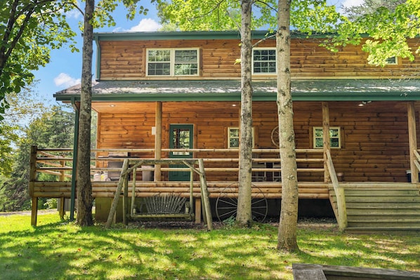 A two-story log cabin with a porch, multiple windows, and a green roof.