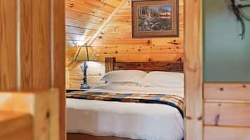 A wooden cabin room with a bed, a nightstand, a lamp, and a framed picture on the wall.