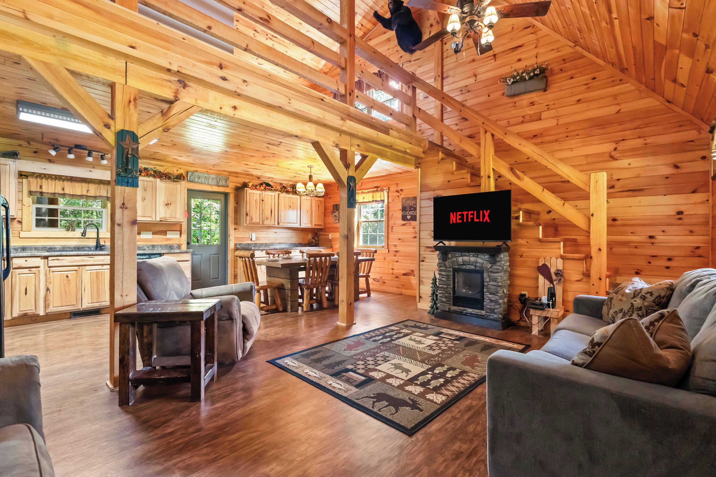 A log cabin interior with a fireplace, a television, wooden furniture, and a kitchen area.