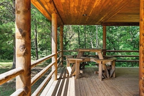 A wooden deck with a picnic table and benches, surrounded by trees.