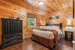 A wooden cabin bedroom with a bed, dresser, window, and wall decorations.