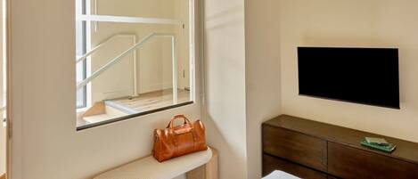 Habitación de hotel con un espejo grande, un banco, un televisor y un aparador de madera.