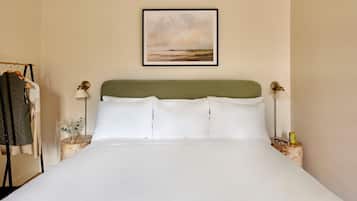 Una cama bien hecha con sábanas blancas, un cabecero verde y dos lámparas de noche.