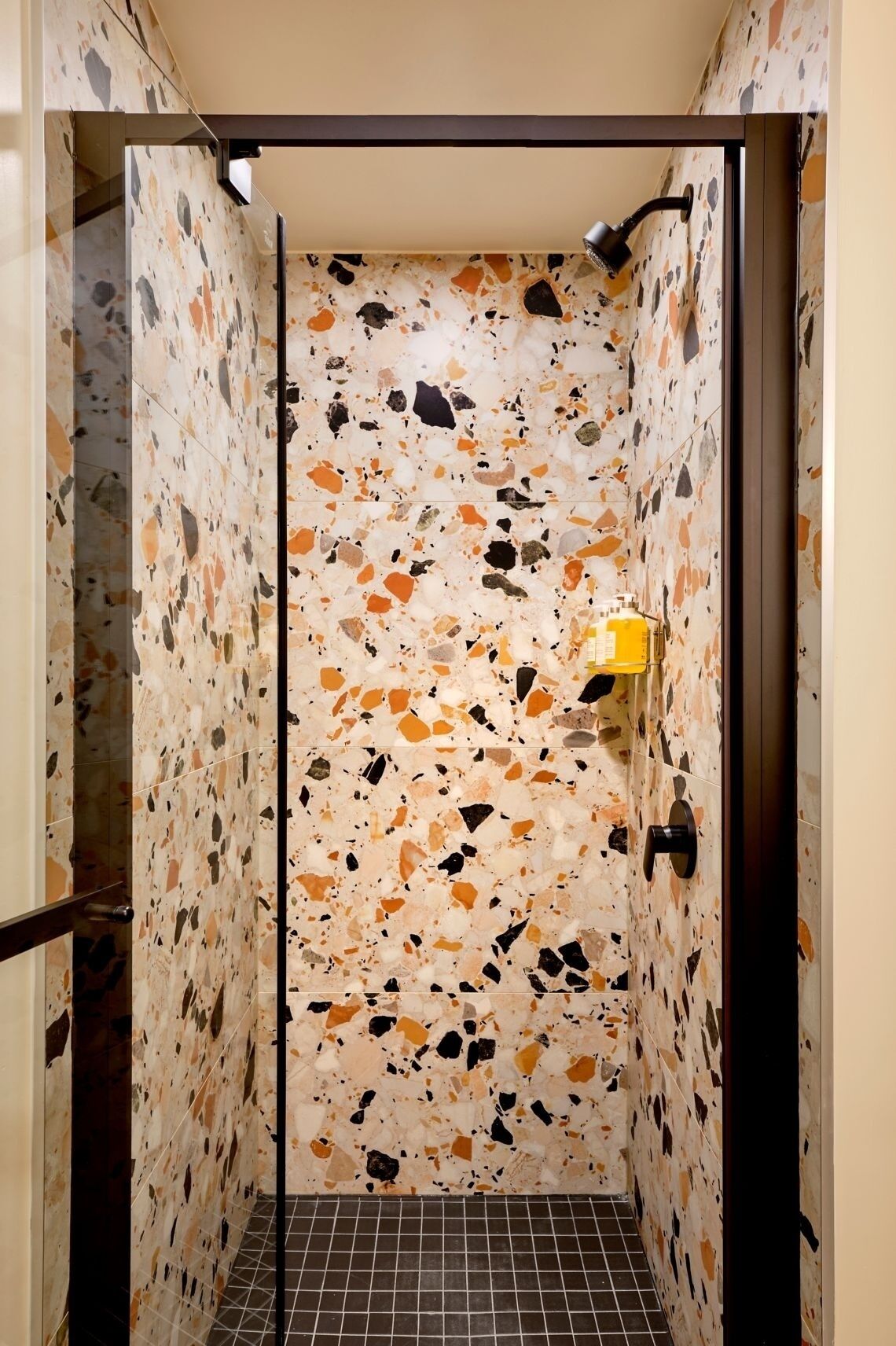 A shower with terrazzo walls and a yellow bottle of shampoo.