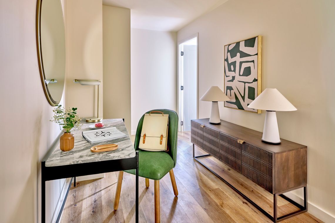 Habitación de hotel moderna con suelo de madera, una butaca tapizada en verde, una mesa de mármol, una consola de madera y un cuadro abstracto de gran tamaño en la pared.