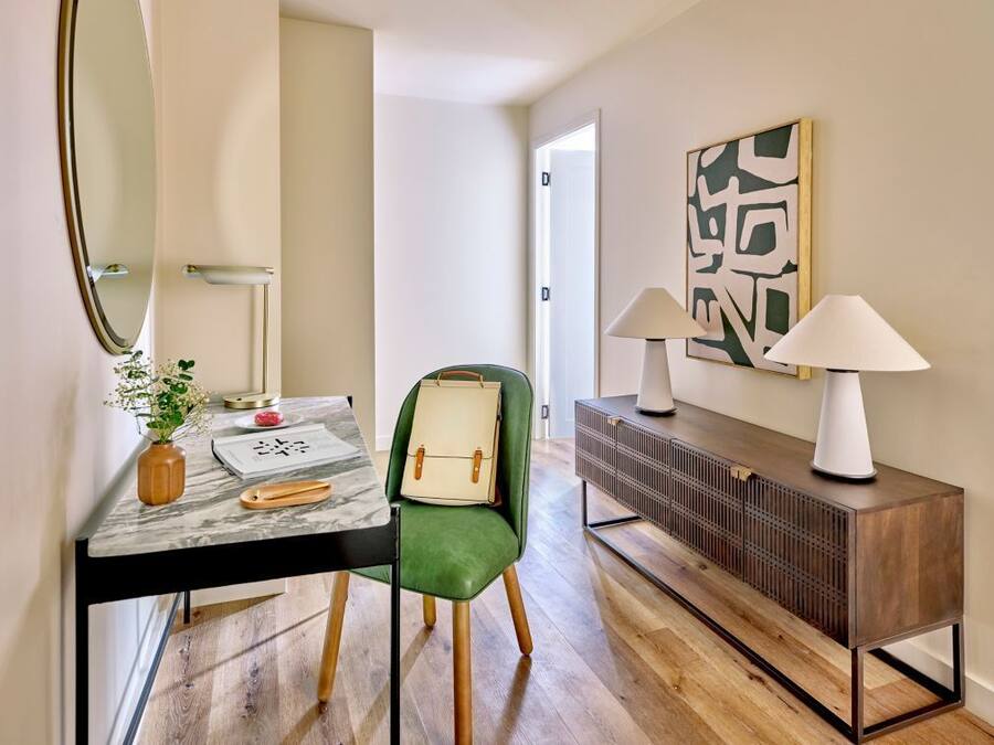 Habitación de hotel moderna con suelo de madera, una butaca tapizada en verde, una mesa de mármol, una consola de madera y un cuadro abstracto de gran tamaño en la pared.