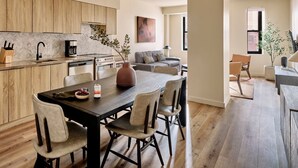 Una cuina moderna amb armaris de fusta, una zona de menjador amb taula fosca i cadires clares, i una sala d'estar amb un sofà gris i una taula de centre.