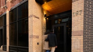 Entrada d'un edifici amb façana de maó, grans finestres i una porta amb el número 197.
