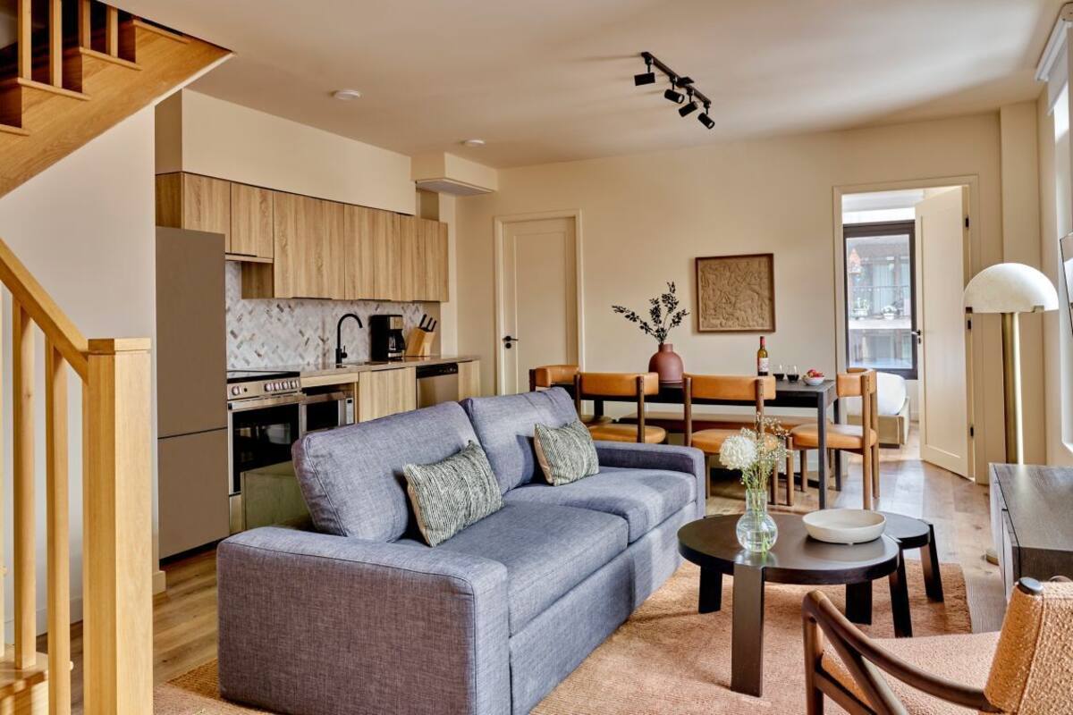 Ein modernes Wohnzimmer mit grauem Sofa, einem Holzespeisetisch und einer Küchenzeile mit Holzschränken und einem Herd.