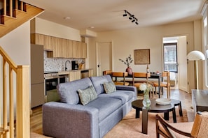 A modern living room with a grey sofa, wooden dining table, and a kitchen area with wooden cabinets and a stove. - Nester Finn St. Lawrence Market (Toronto)