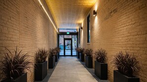 Un passadís amb parets de maó, planters negres amb plantes i un sòl de rajoles.