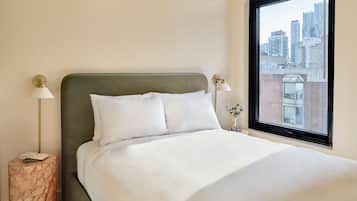 Een net opgemaakt bed met witte lakens en een groen hoofdeinde in een hotelkamer met uitzicht op de stad.