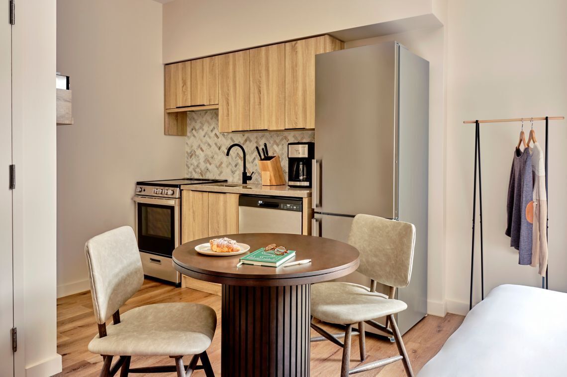 A compact kitchen with modern appliances, a dining area with two chairs, and a clothing rack.