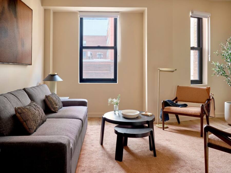 Una sala de estar con sofá, una mesa redonda, una silla y una ventana con vistas a un edificio.