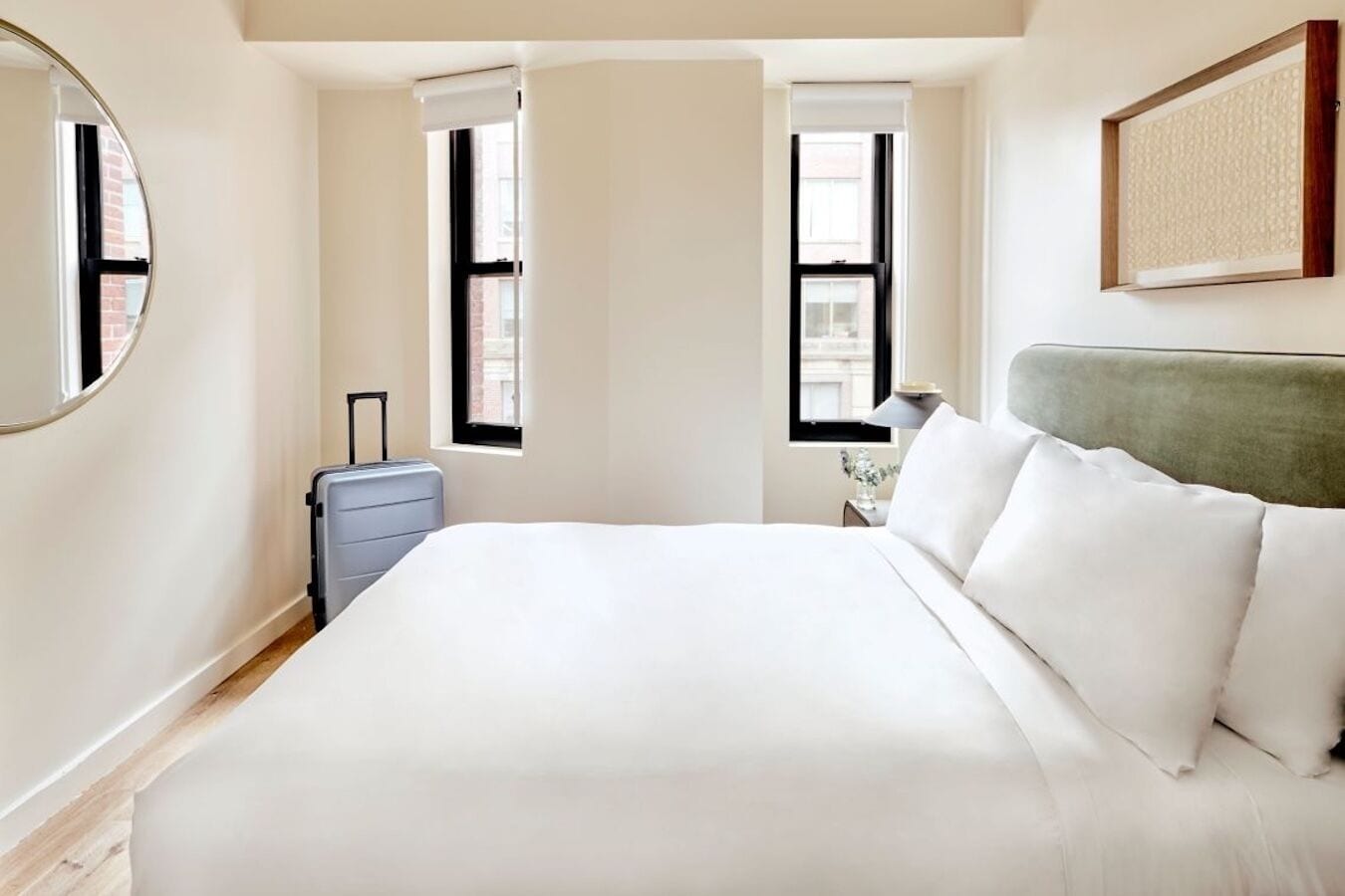 A hotel room with a large bed, a suitcase, and two windows.