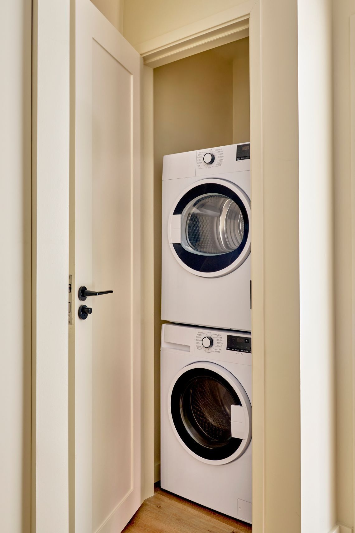 A laundry room with two stacked washing machines, a door, and a wooden floor.
