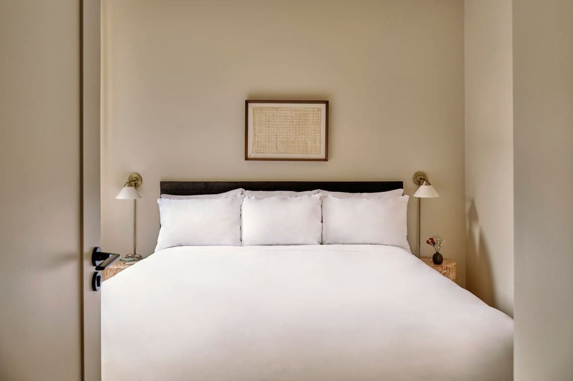 Un lit bien fait, avec du linge de lit blanc, une tête de lit sombre et deux lampes de chevet.