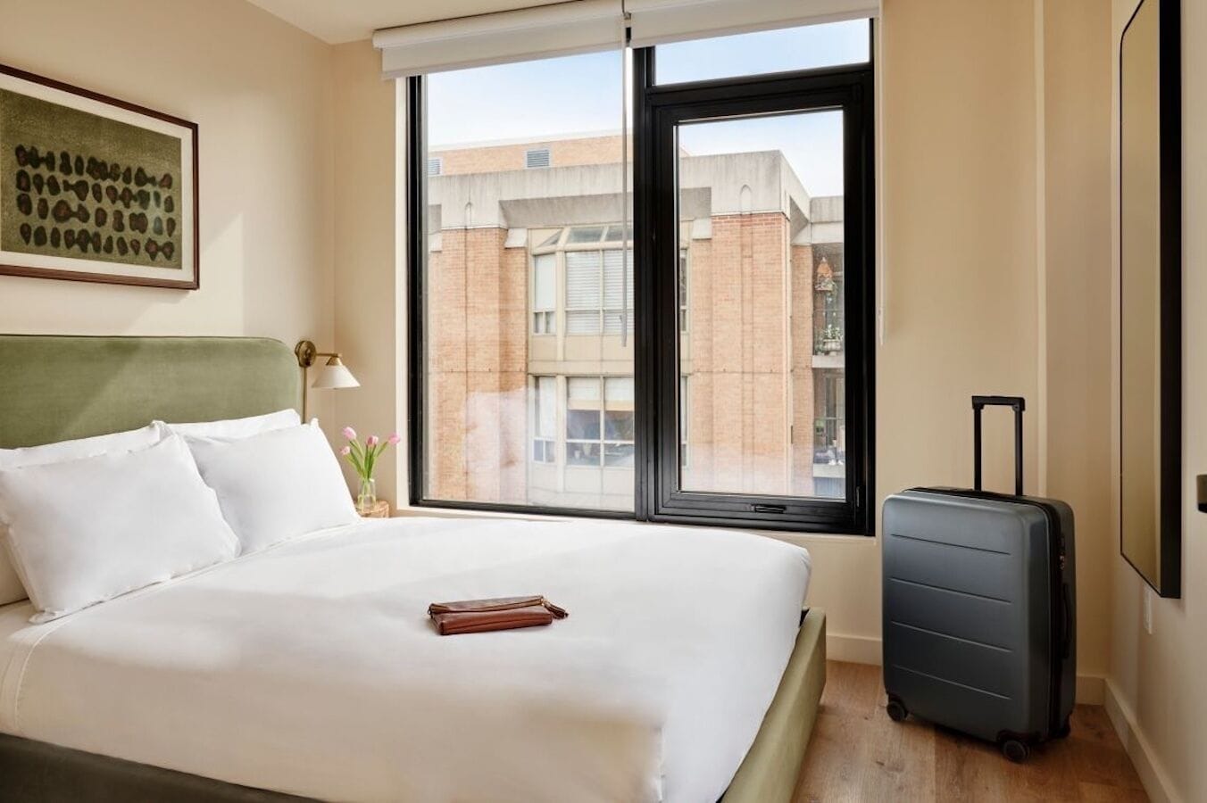 A hotel room with a bed, a suitcase, and a window with a view of buildings.