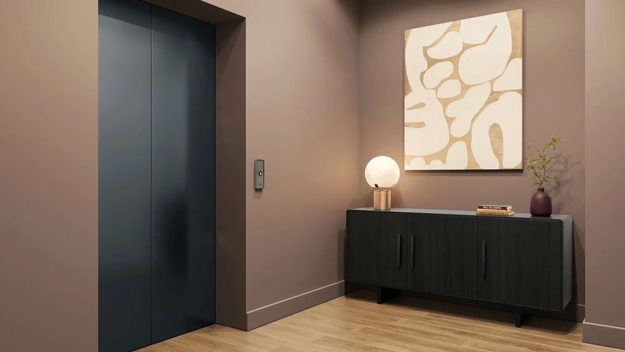 Un couloir moderne avec une porte sombre, un luminaire fixé au mur, une console ornée d’objets décoratifs et une œuvre d’art abstraite.