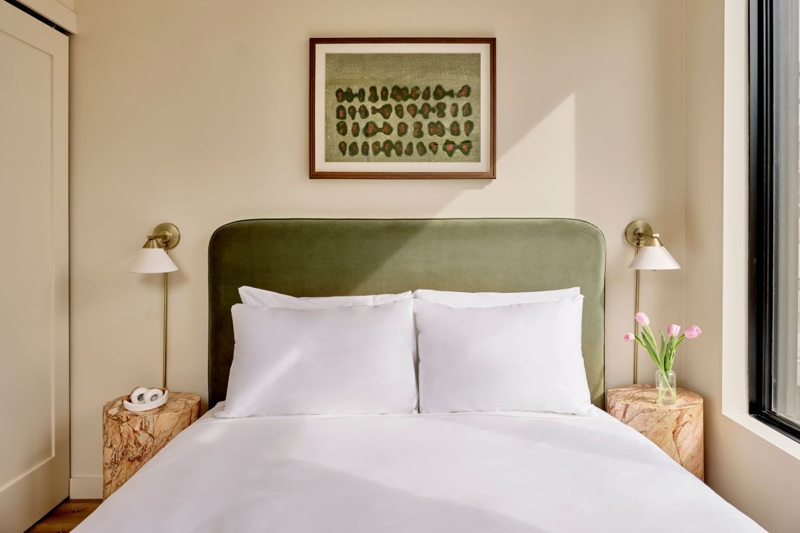 A neatly made bed with white linens, a green upholstered headboard, and two bedside tables with lamps.