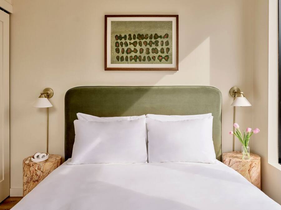 A neatly made bed with white linens, a green upholstered headboard, and two bedside tables with lamps.