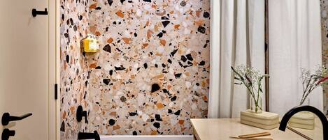 Un baño moderno con suelo de terrazo, bañera, lavamanos y espejo.