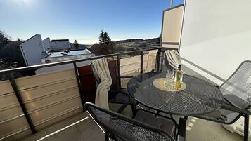 A balcony with a table and chairs, a bottle of wine, and a view of a swimming pool and buildings.