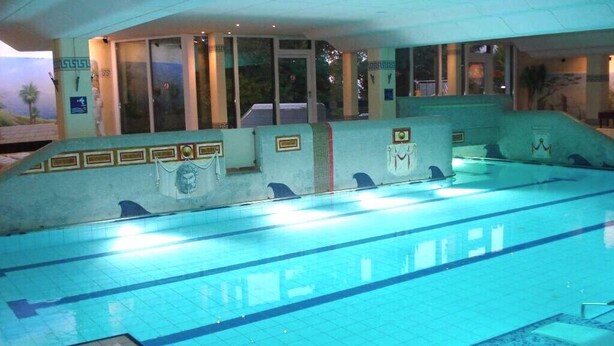 Una piscina interior con carriles delimitados, zona de vestuarios y un área de descanso con sillones reclinables.