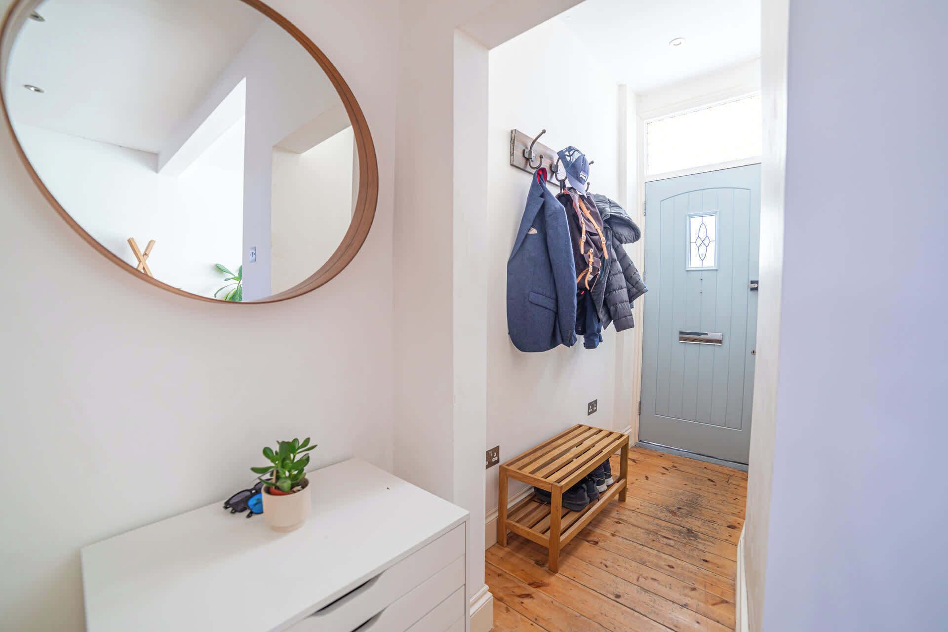 A hallway with a mirror, a coat rack with jackets, a small wooden bench, and a door.