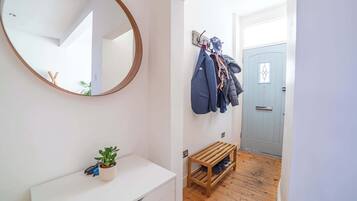 A hallway with a mirror, a coat rack with jackets, a small wooden bench, and a door.