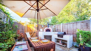 Un patio al aire libre con mesa de madera, sillas, una parrilla y un horno para pizza.