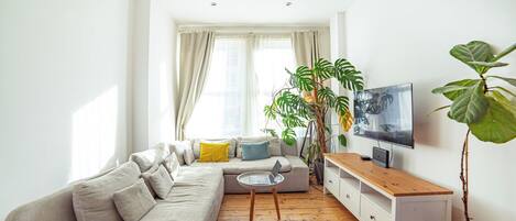 A modern living room with a sofa, coffee table, TV, and plants.