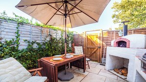 Un patio al aire libre con una mesa lista para comer, un horno de pizza y una valla de madera con plantas.
