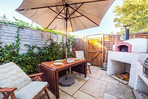 Un patio al aire libre con una mesa lista para comer, un horno de pizza y una valla de madera con plantas.