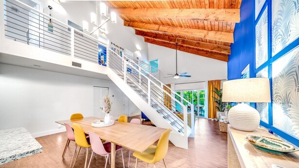 A modern interior with a wooden dining table, yellow chairs, a staircase, and a blue accent wall. - Sunset Haven w/ Saltwater Pool, Arcade Mins to Beach (Delray Beach)