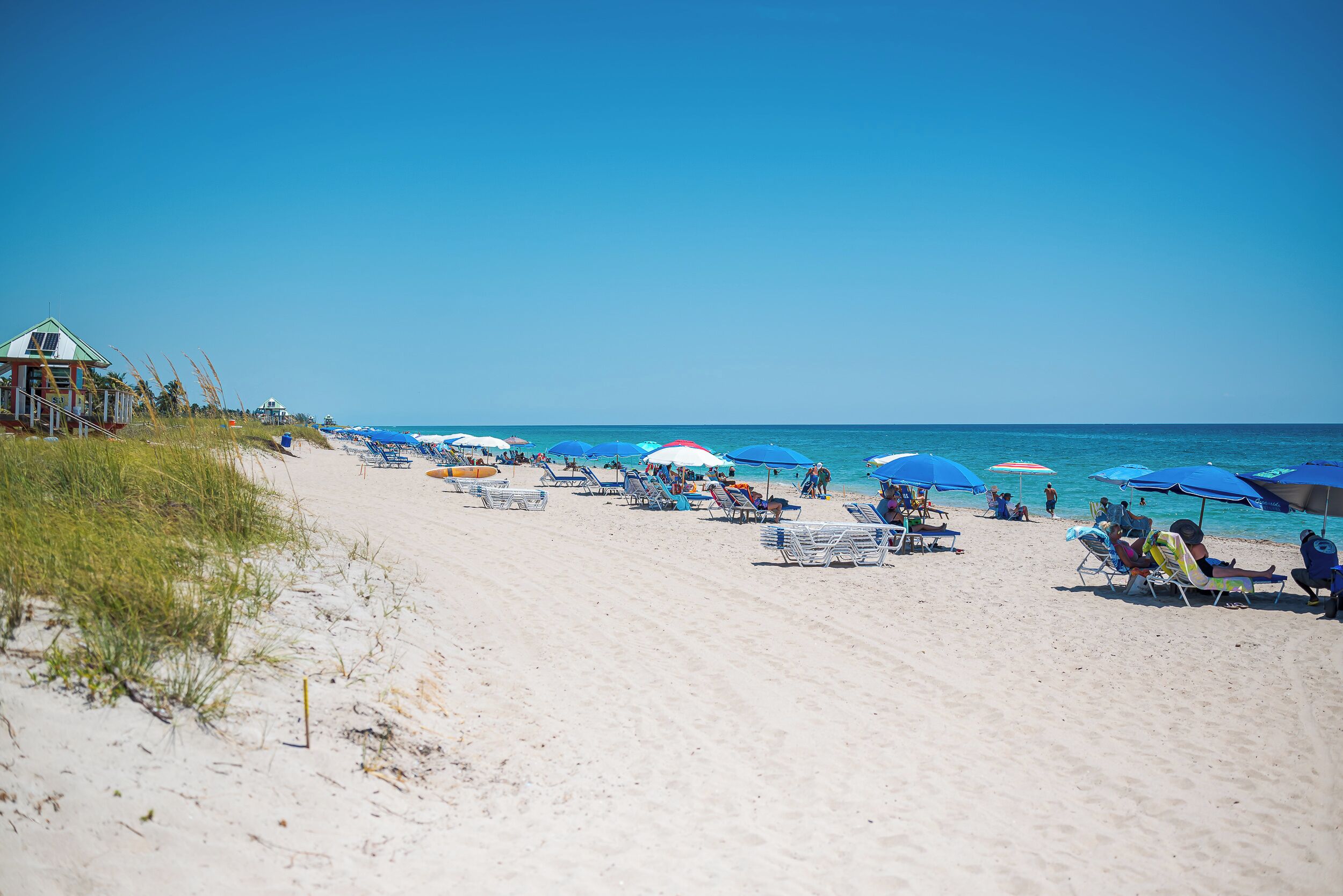 A beach with sun loungers and umbrellas, a lifeguard tower, and the ocean.